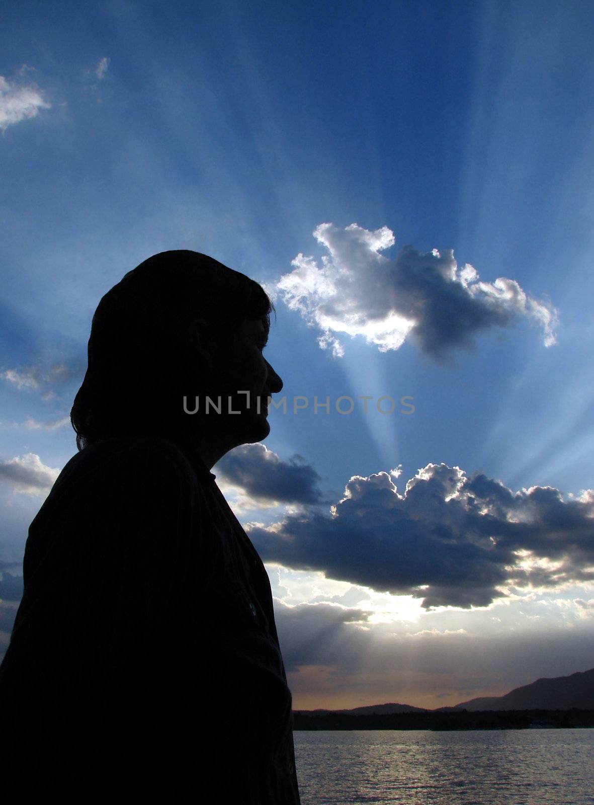 Close-up of a woman head in silhouette with sun-rays in the clouds as a background