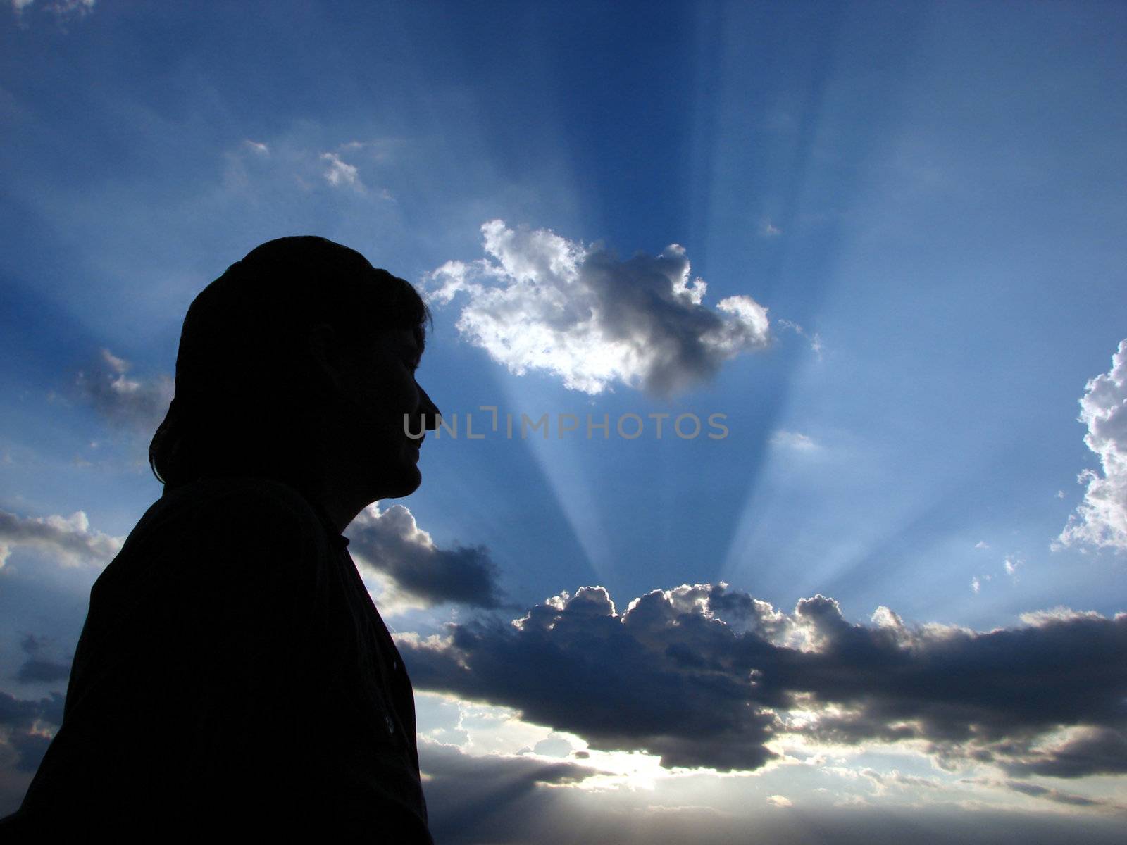 Close-up of a woman head in silhouette with sun-rays in the clouds as a background