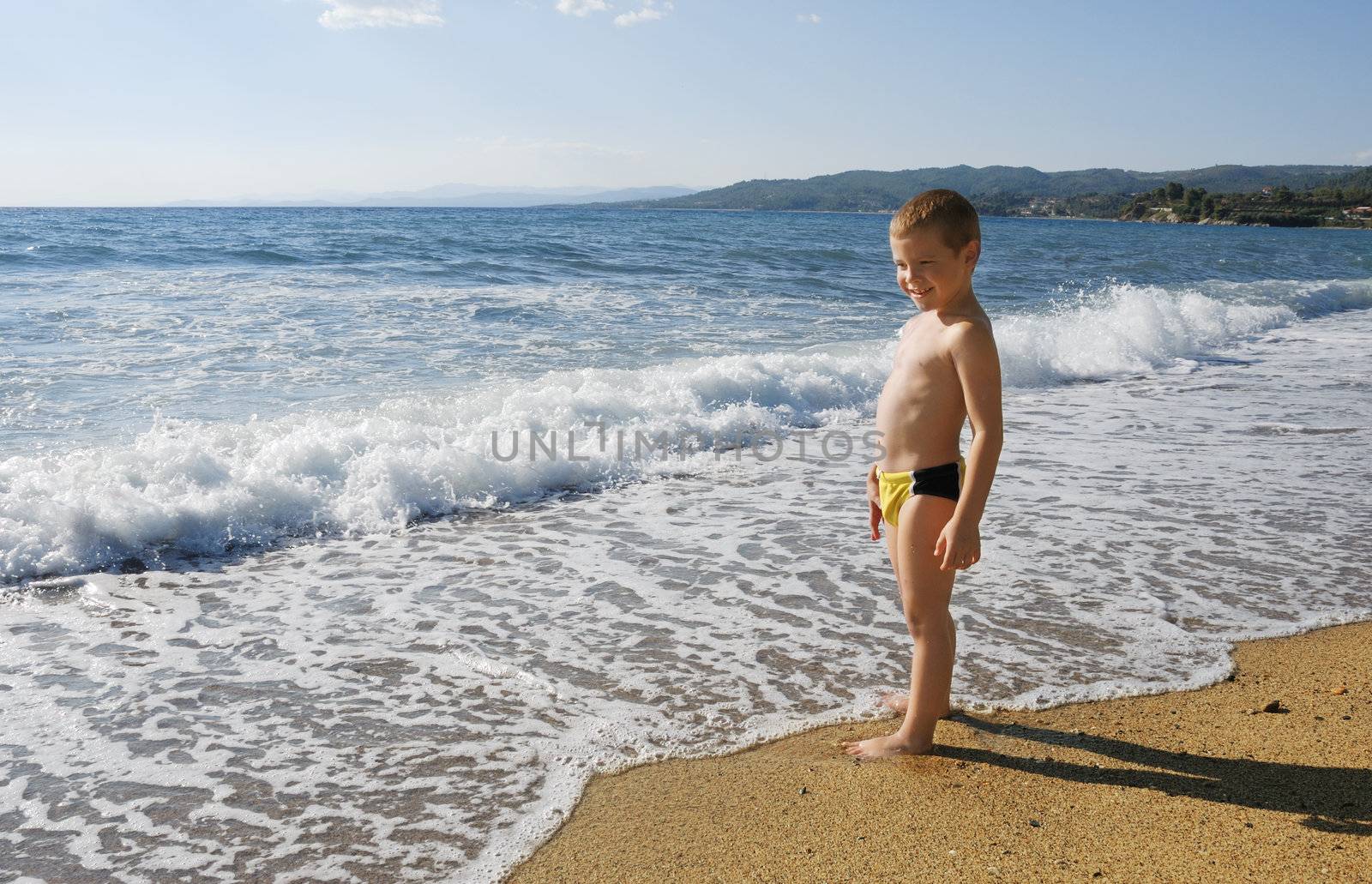 a boy is standing on a beach looking at sea wave