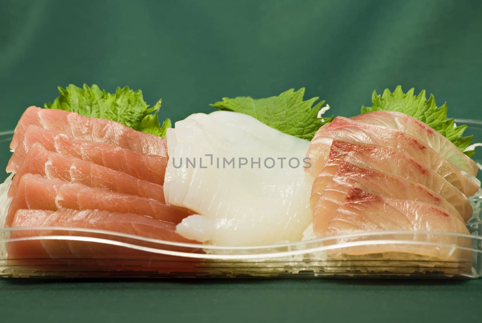 plate of traditional Japanese food called sasimi; different raw fish slices lay on cut vegetables; this is macro-image sharp focus is on central part