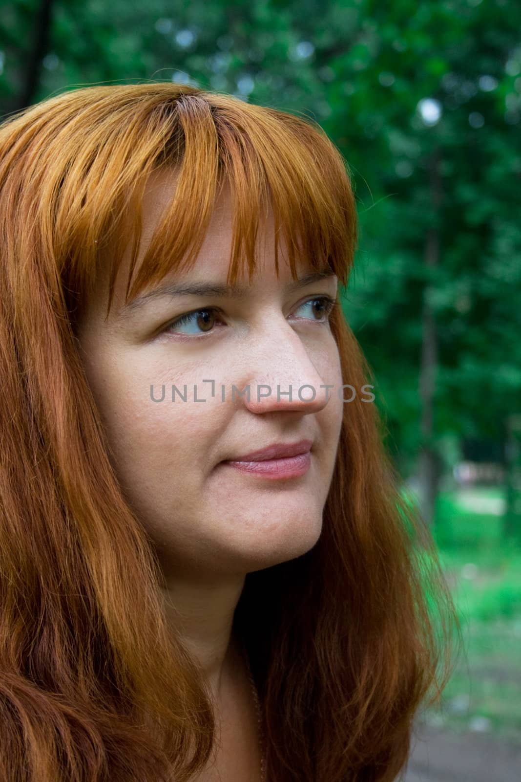 Portrait of the woman with red hair in dark blue clothes against green plants