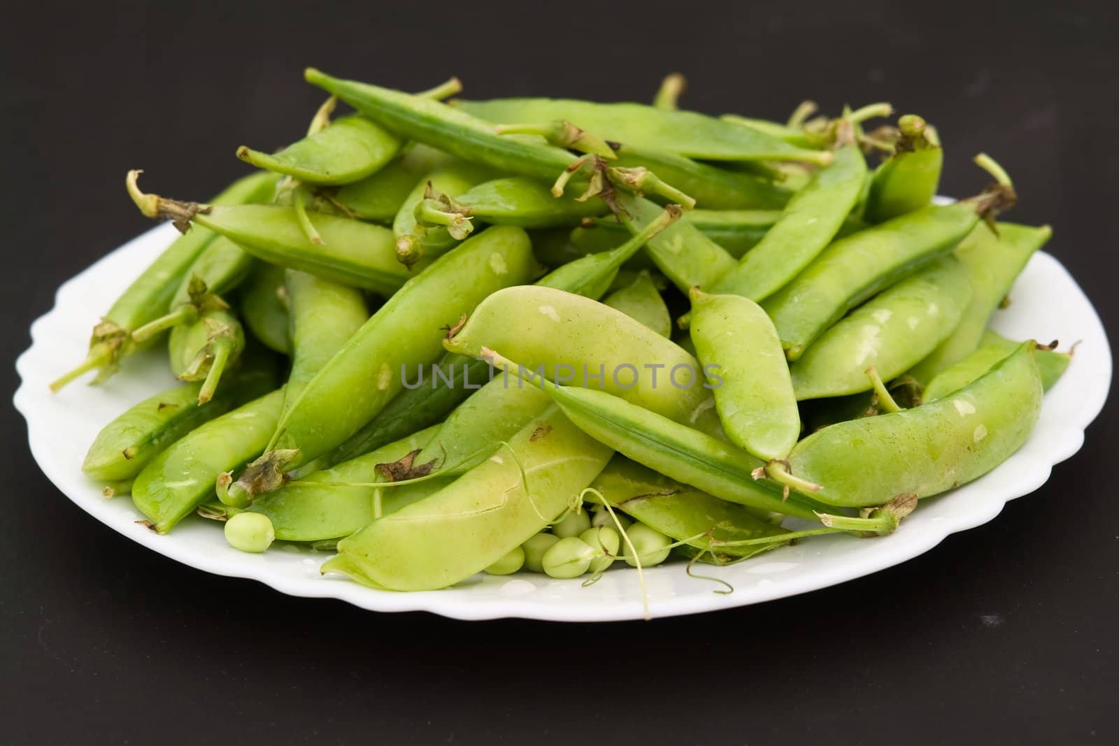 Peas pods on a white plate on a black background