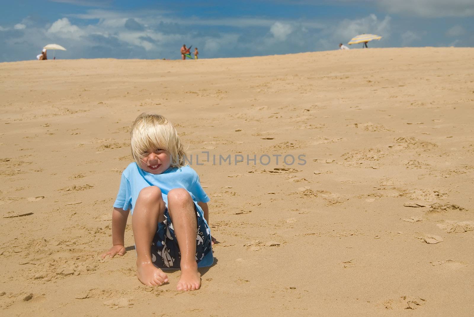 a boy sitting on the beach on a sunny day