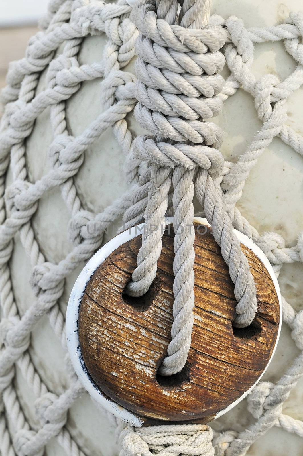 Close-up of an old block on a sailboat with a bumper covered by a rope net in background