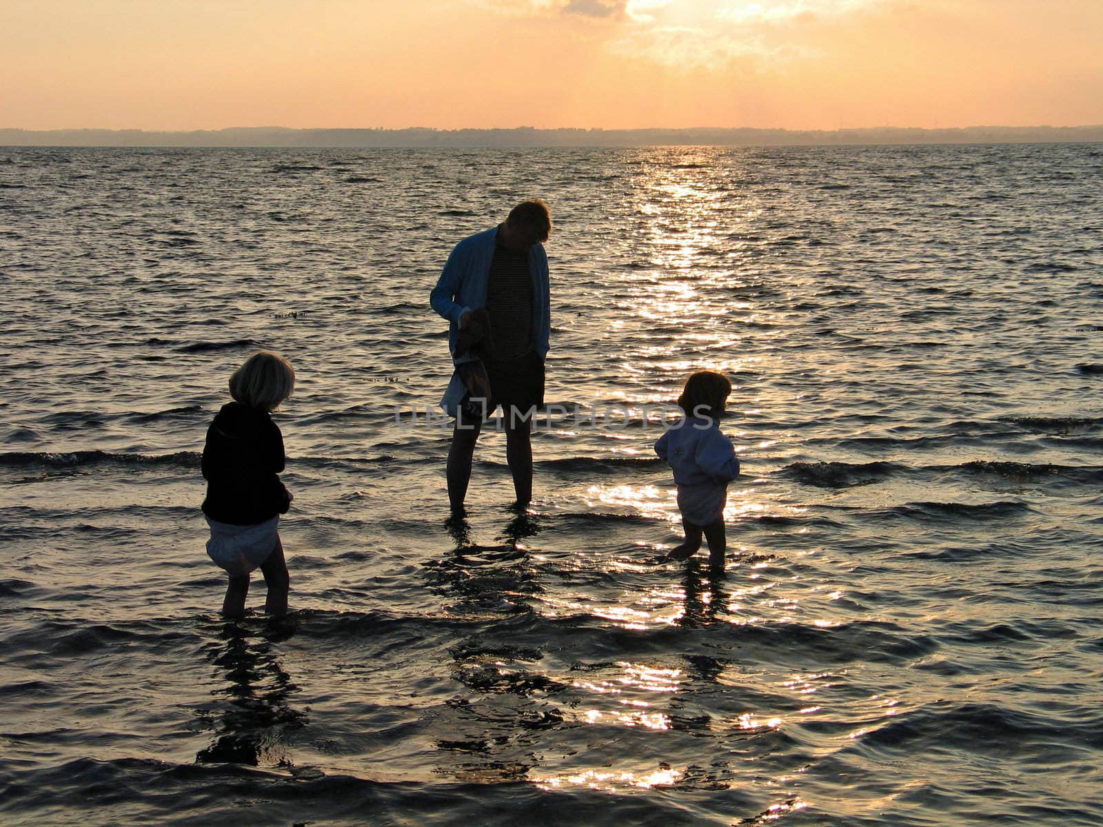 Family - father and girls play in the water in sunset time