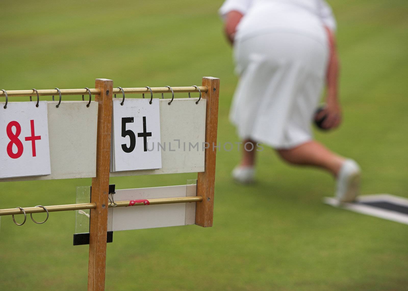 A lady playing lawn bowls and the scoreboard.