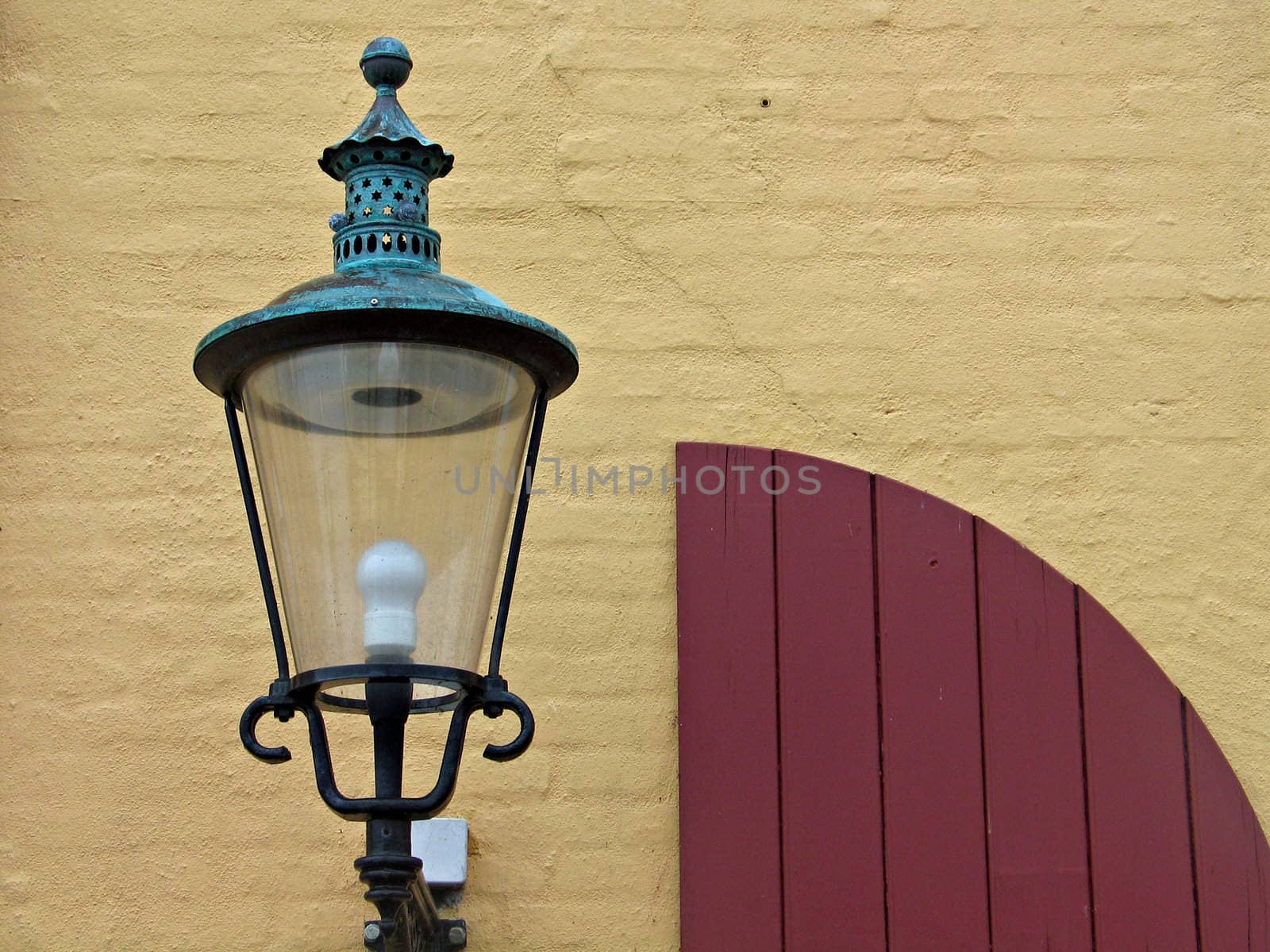 Old European copper street lamp in front of yellow brickes wall