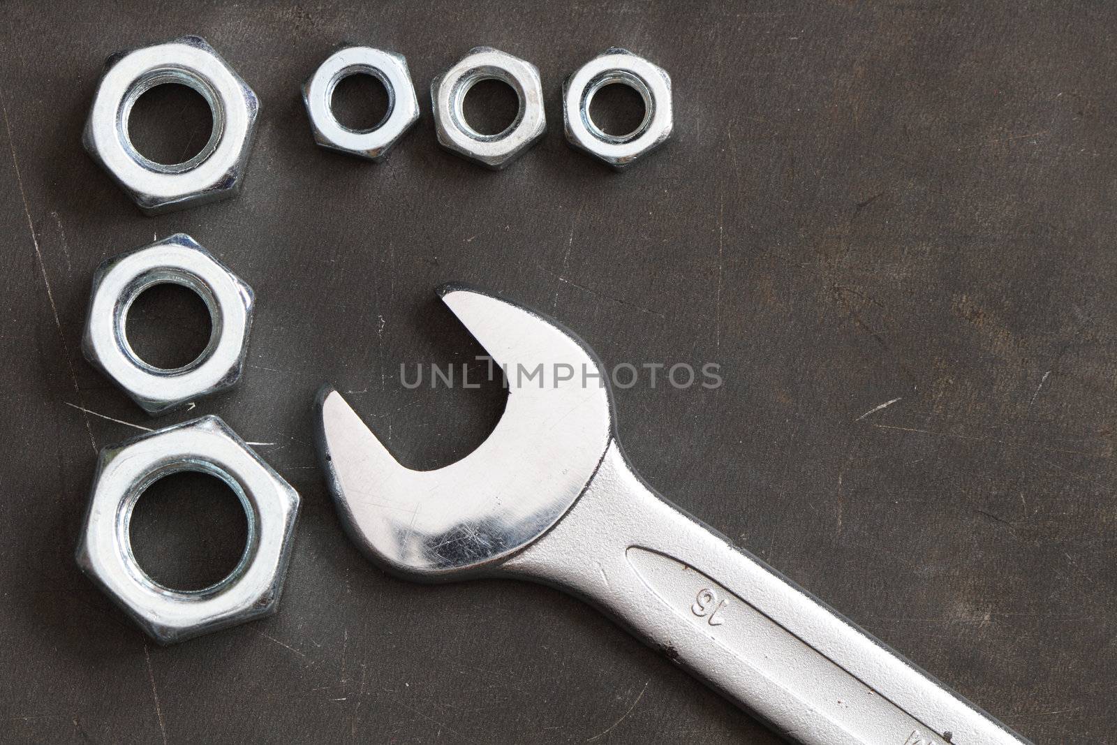 Closeup of spanner wrench and few screw nuts on dark metal background