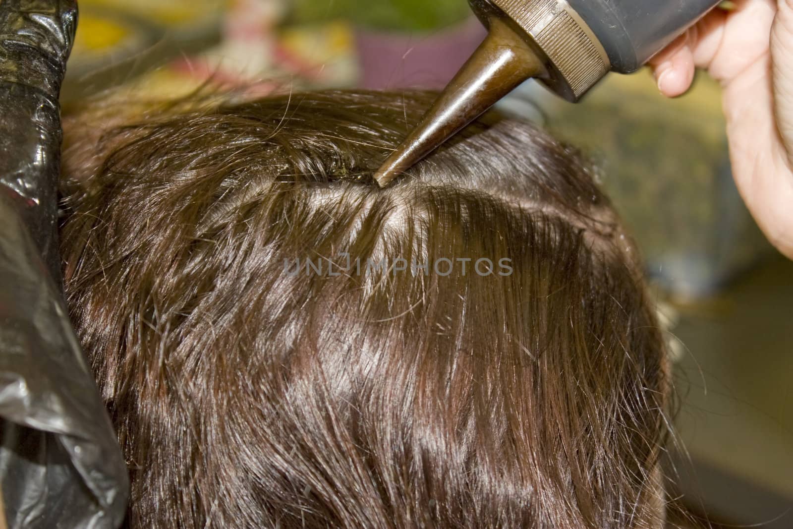 A closeup of a woman getting hair dye applied to her scalp.