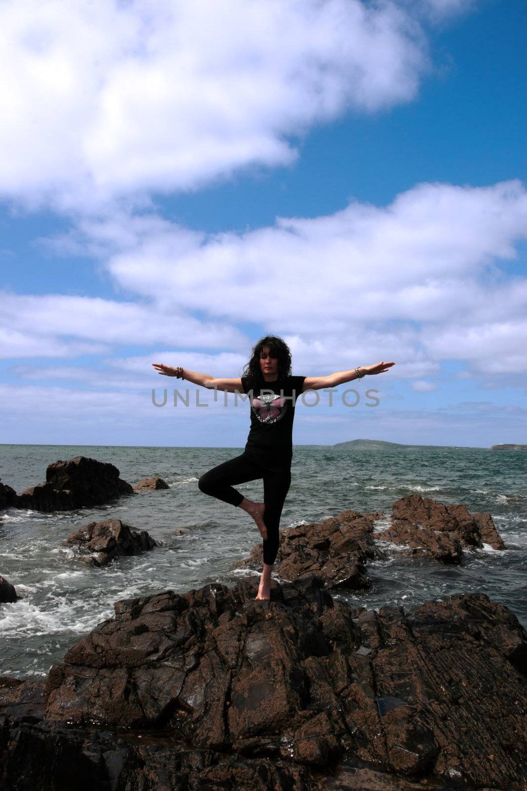 a beautiful woman doing yoga on the edge of the rocks with waves splashing to show a healthy way to live a happy and relaxed lifestyle in a world full of stress