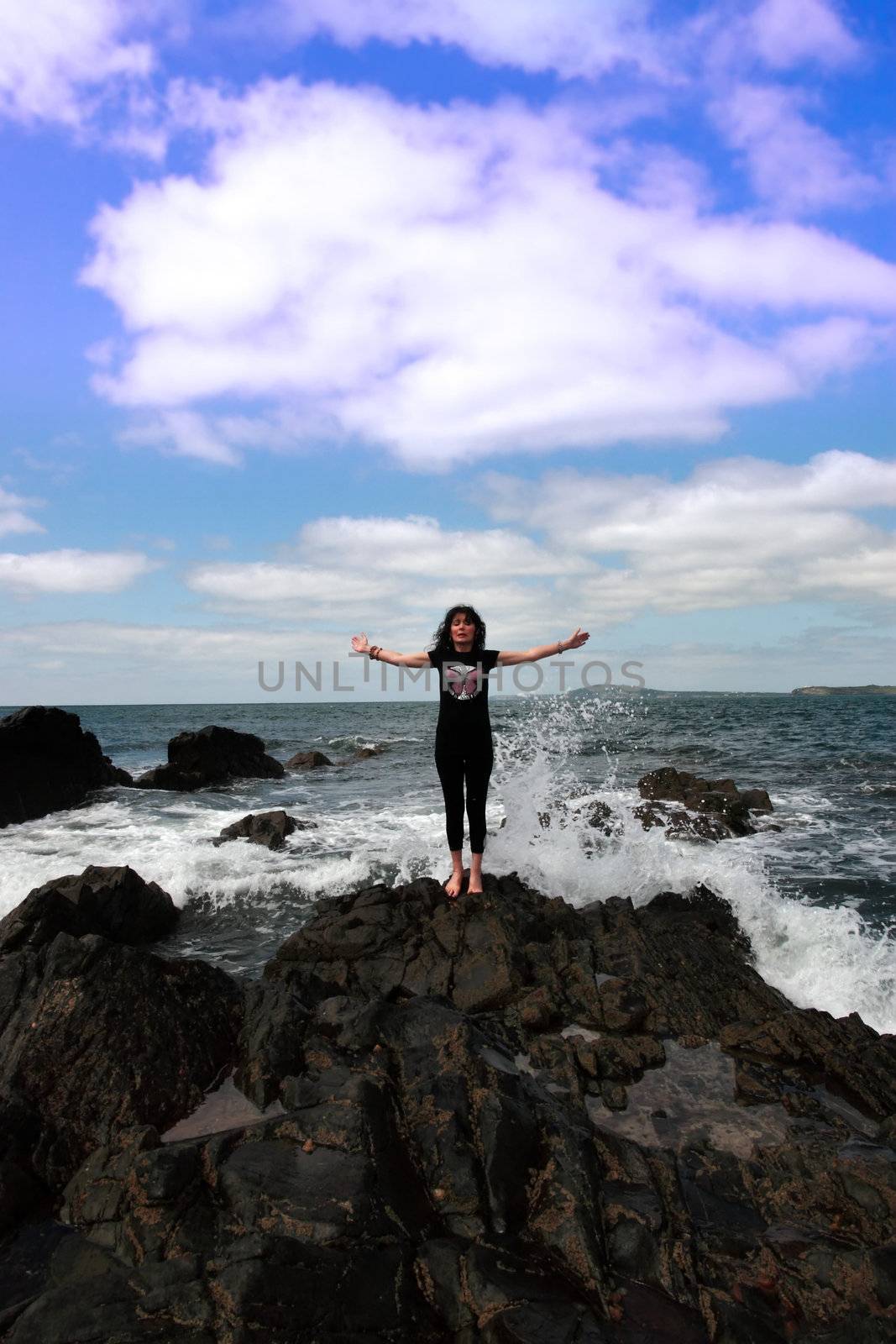 a beautiful woman doing yoga on the edge of the rocks with waves splashing to show a healthy way to live a happy and relaxed lifestyle in a world full of stress