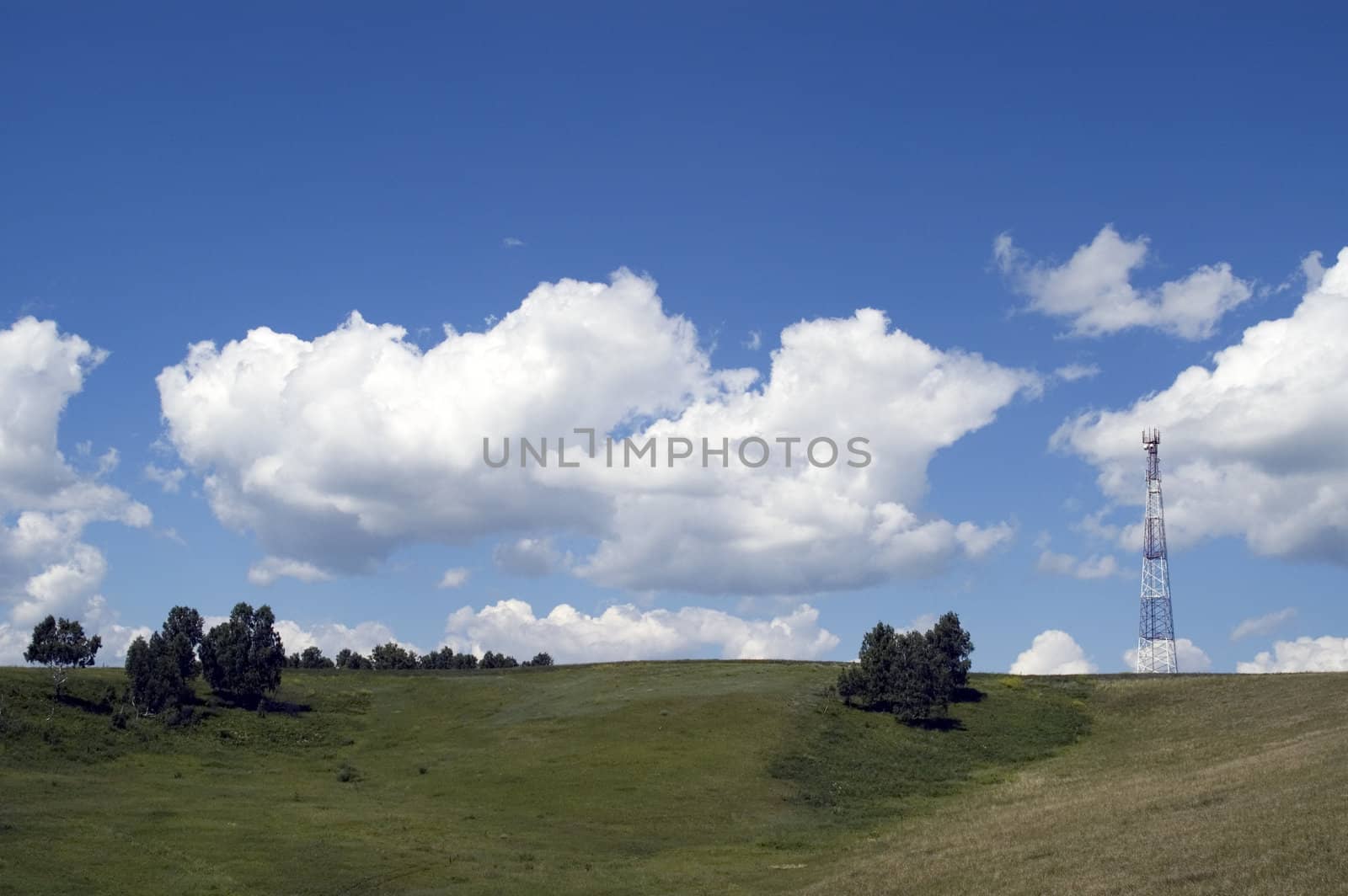 Telecommunication tower on the green field with blue sky.