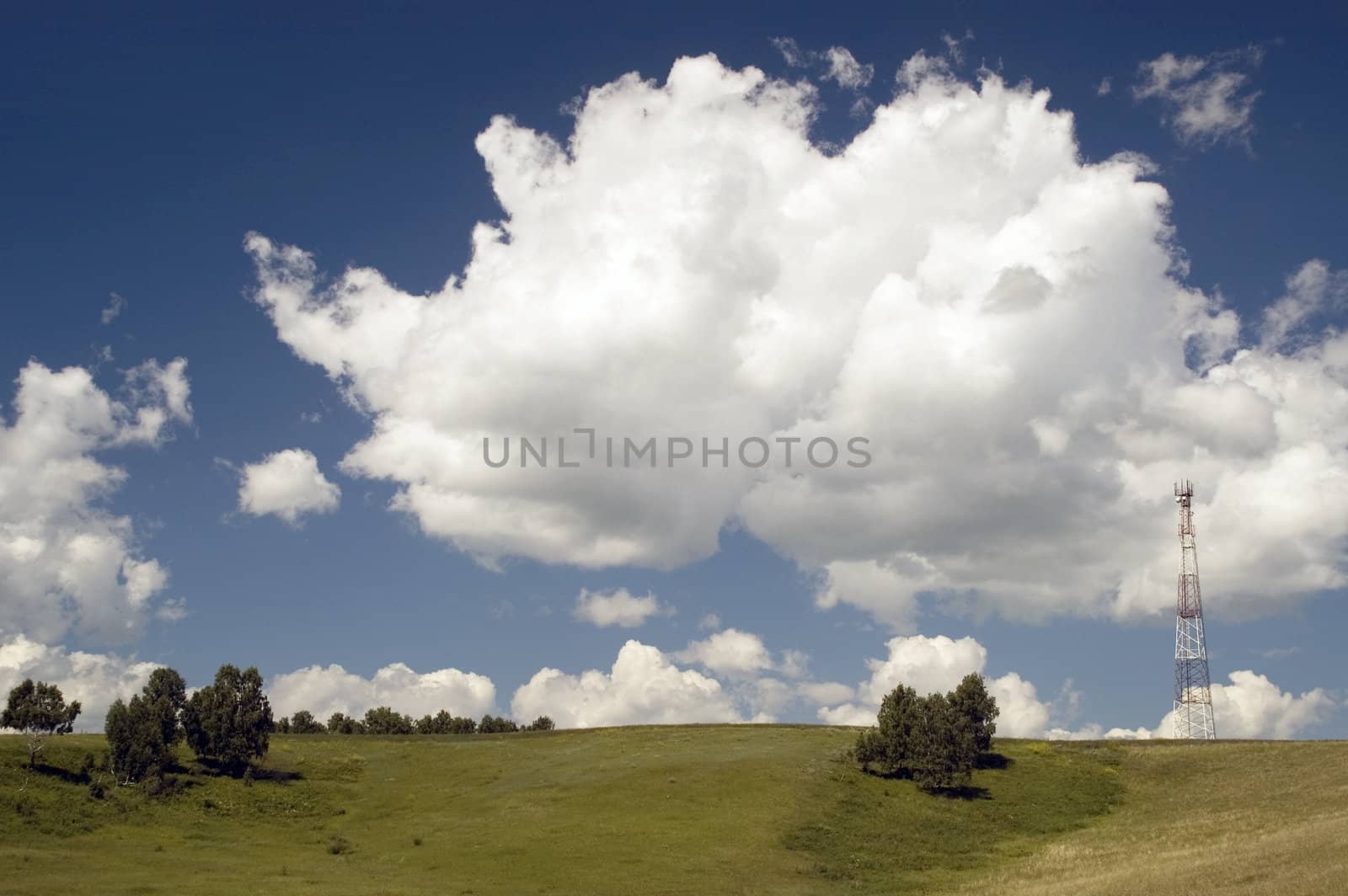 Telecommunication tower on the green field with blue sky.
