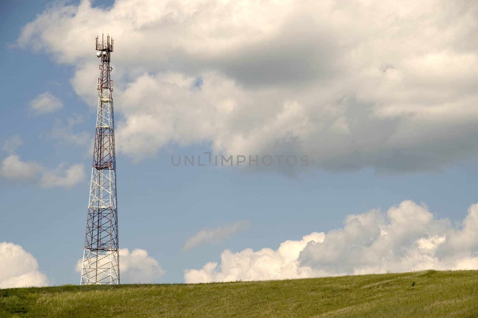 Telecommunication tower on the green field with blue sky.