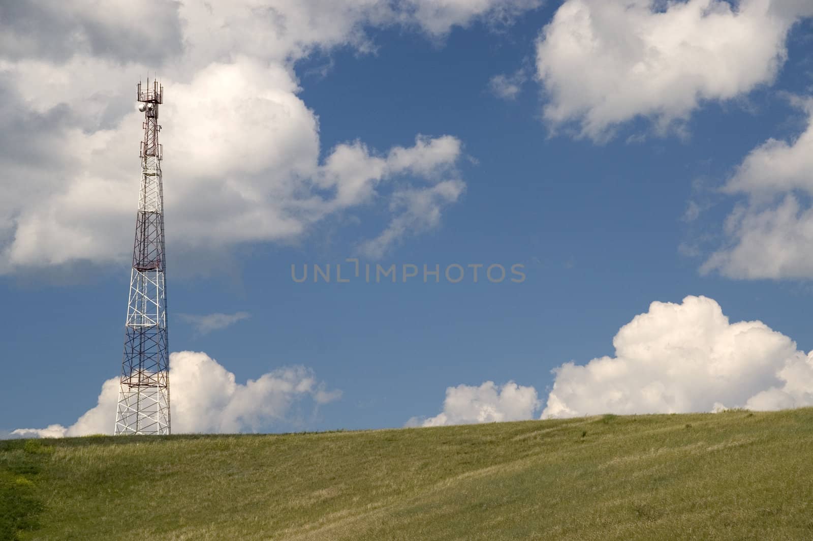 Telecommunication tower on the green field with blue sky.
