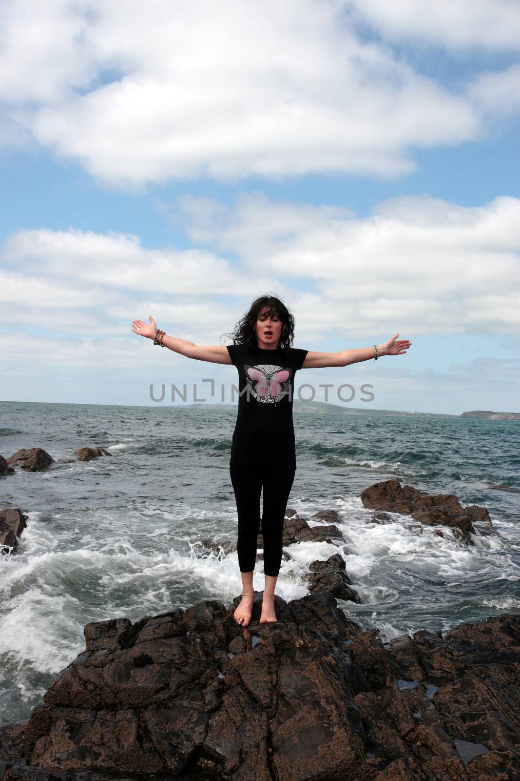 a beautiful woman doing yoga on the edge of the rocks with waves splashing to show a healthy way to live a happy and relaxed lifestyle in a world full of stress