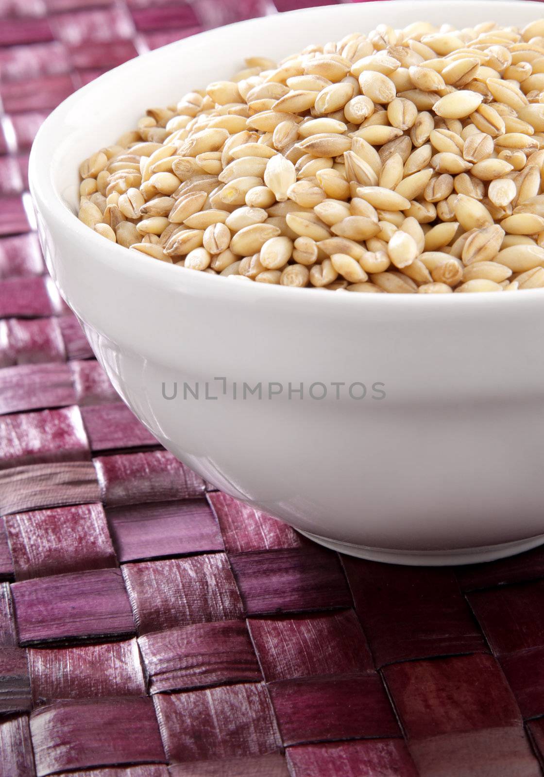 A bowl of organic barley on purple surface.
