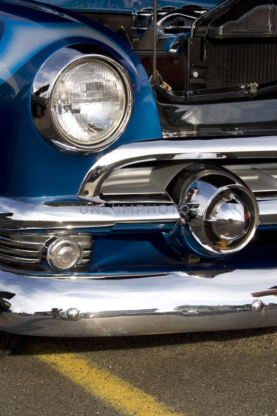 A closeup of the headlight and front bumper on a vintage car.