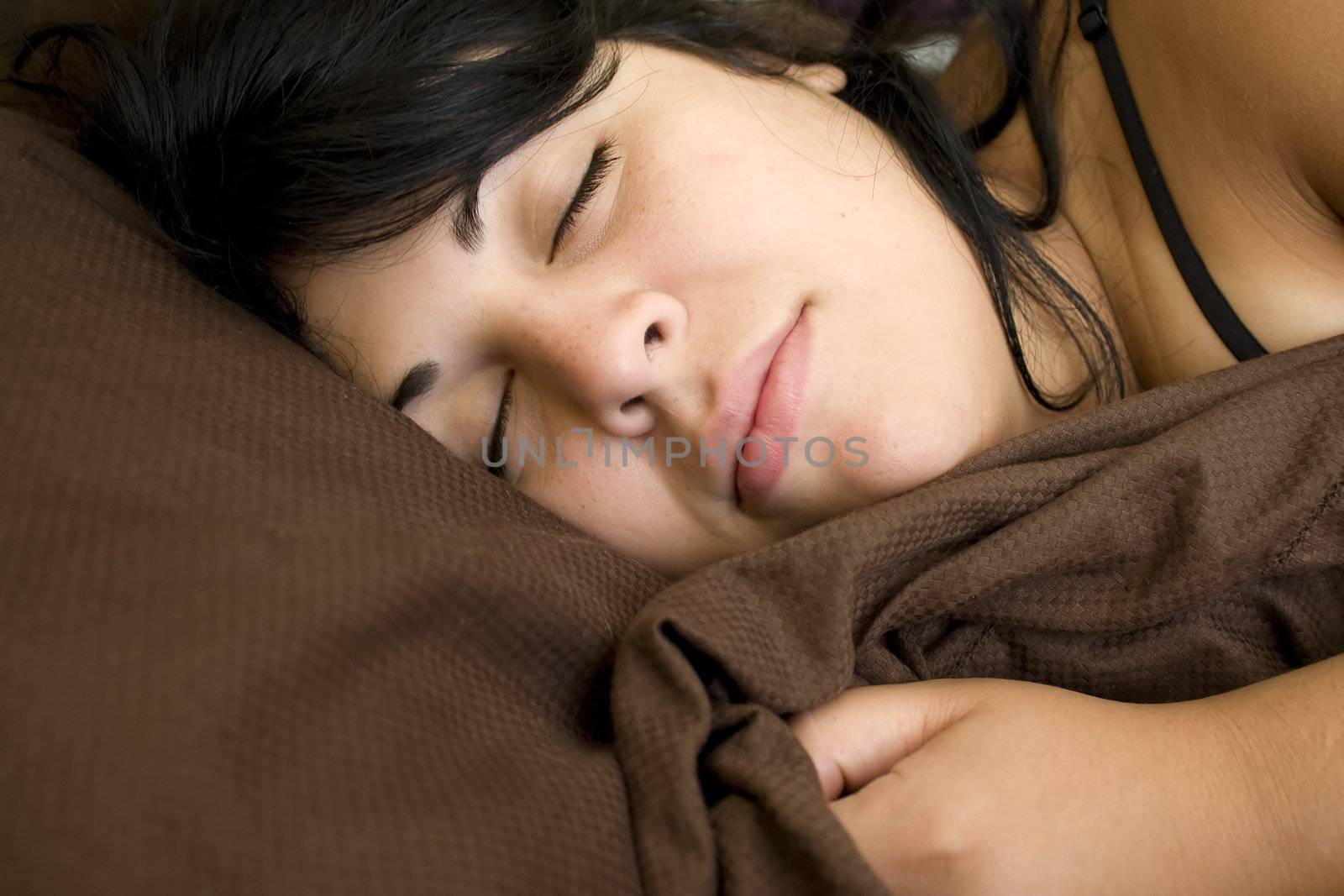 A young brunette woman is fast asleep in her bed.