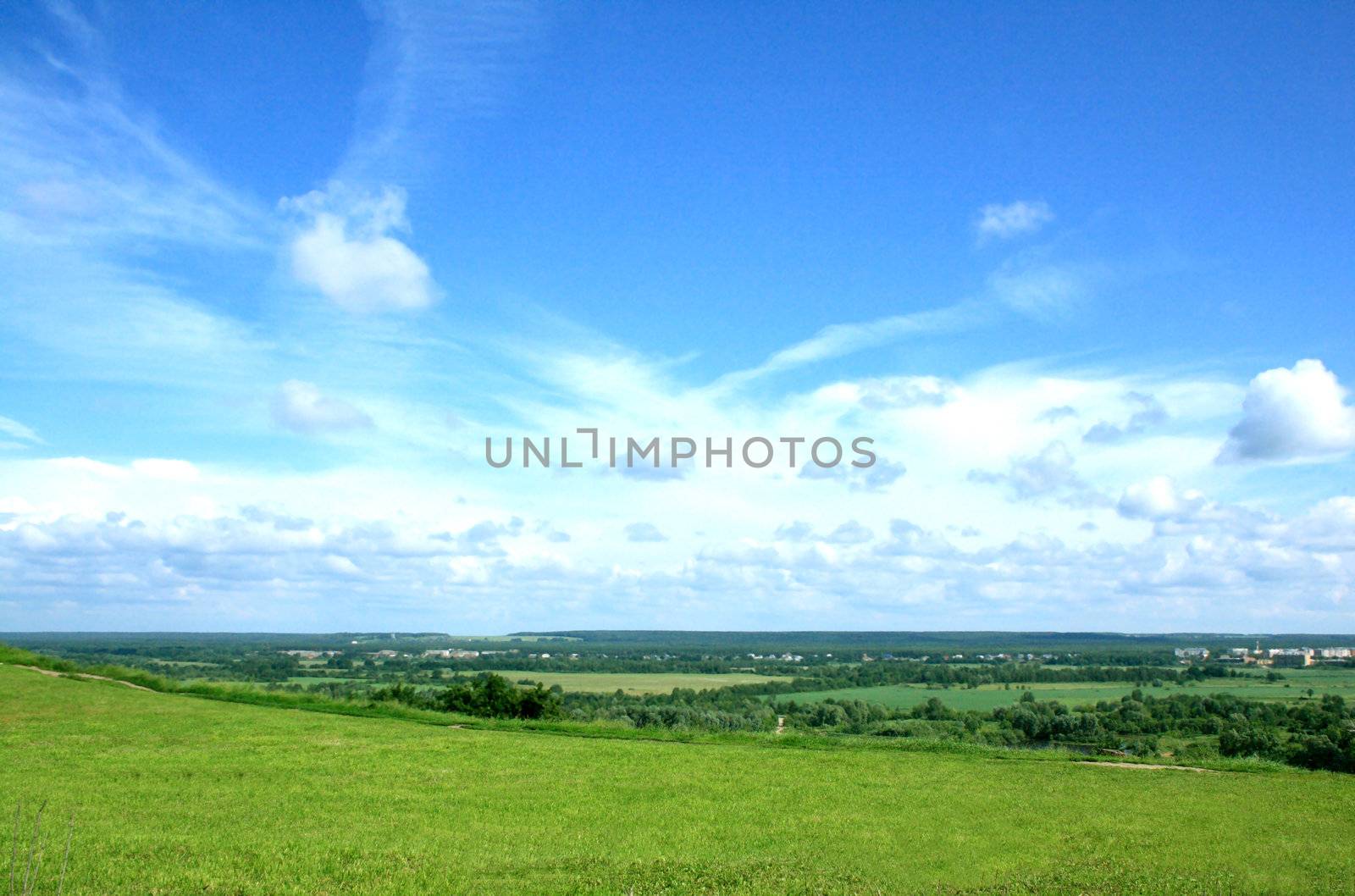 Summer landscape with a wide green valley and the blue sky with white clouds. 