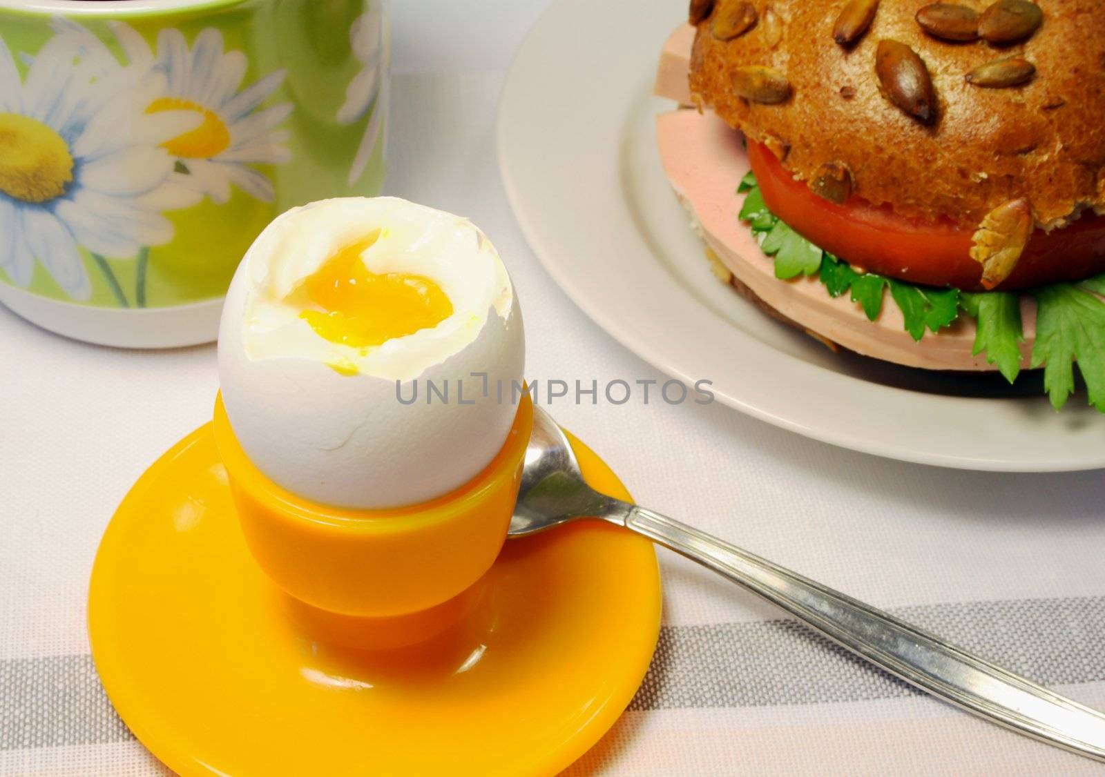Breakfast from cooked eggs, a sandwich with sausage, a tomato and a parsley and cups of tea.