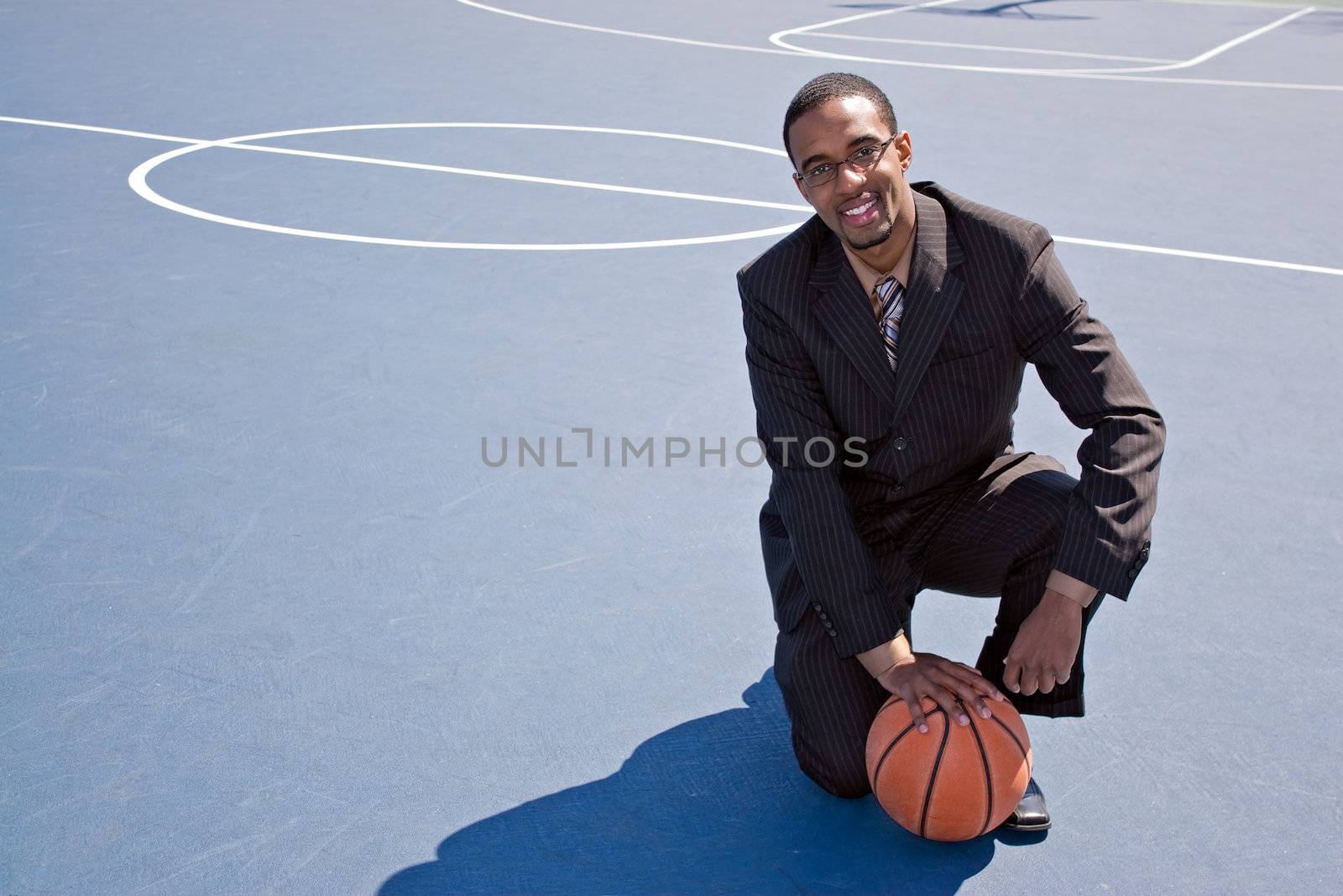 A young African American man in a business suit posing on the basketball court with a ball.  Works great for coaching or recruitment concepts.