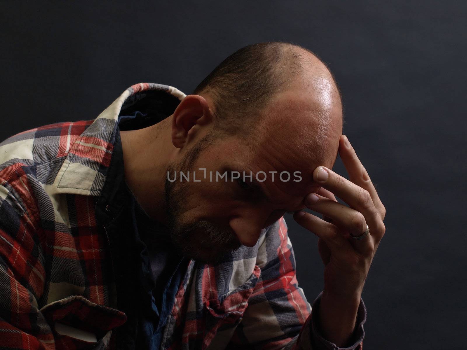 A man in deep thought holds his head in his hand. Over black.