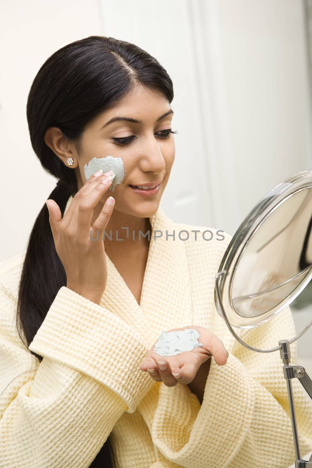 Woman applying facial treatment. by iofoto