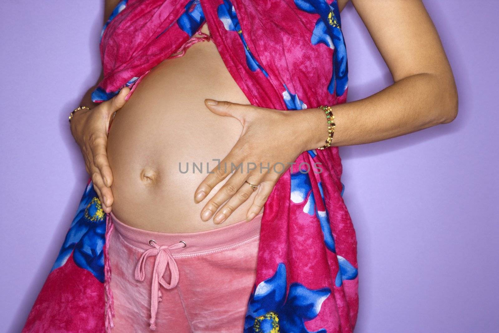 Close up portrait of expecting female with hands on stomach.