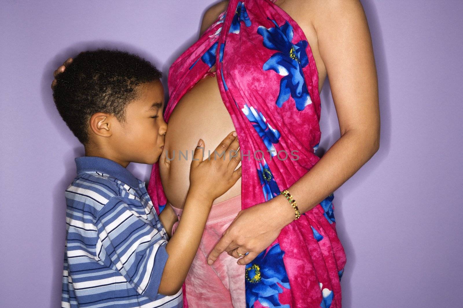 Portrait of expecting female with son kissing stomach.