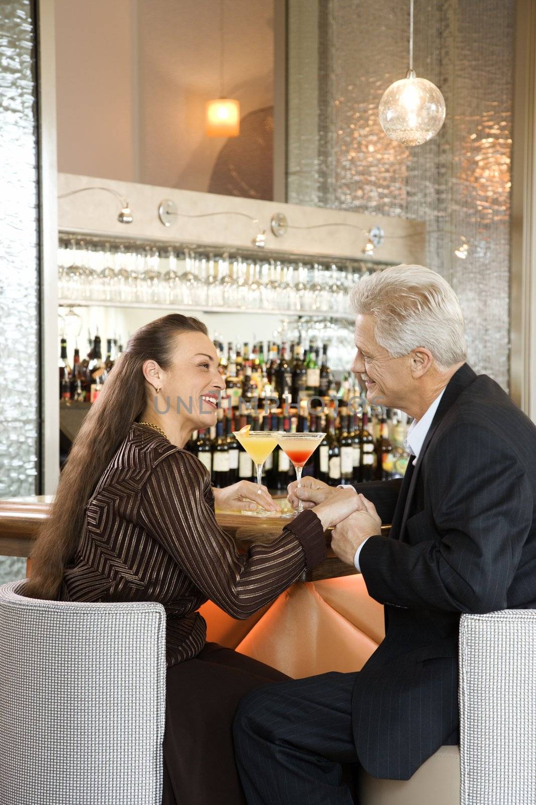 Caucasian mature adult male and prime adult female sitting at bar holding hands.