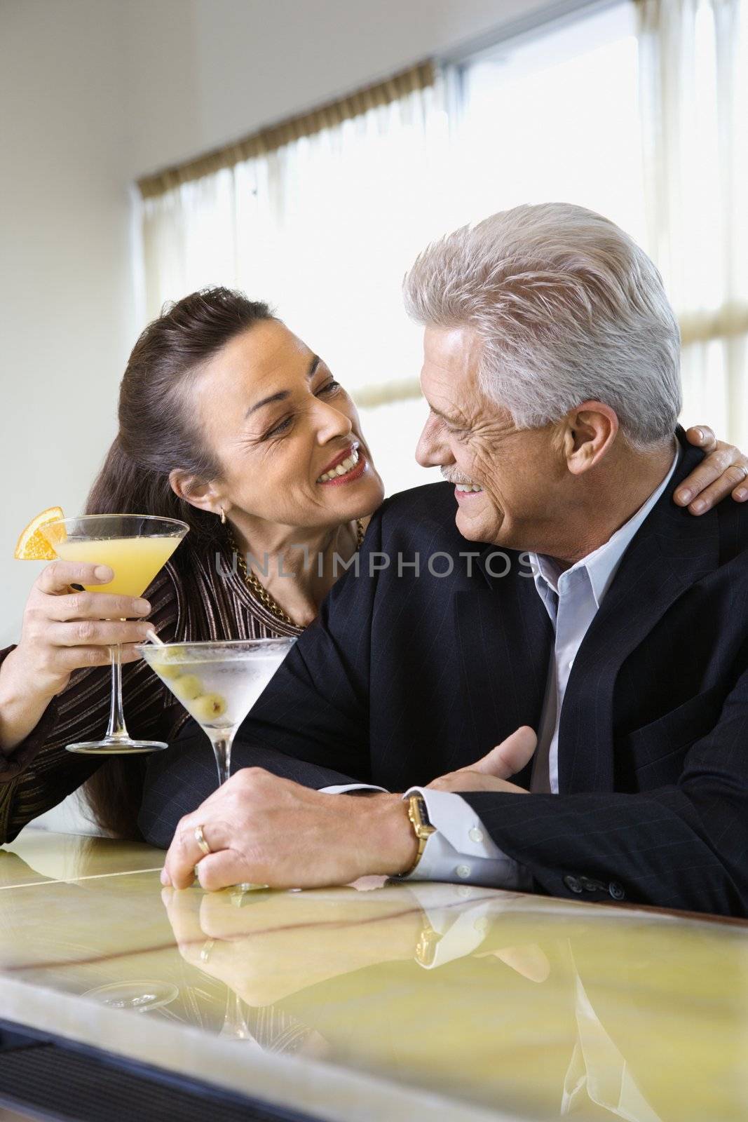 Caucasian mature adult male and prime adult female sitting at bar with cocktails.