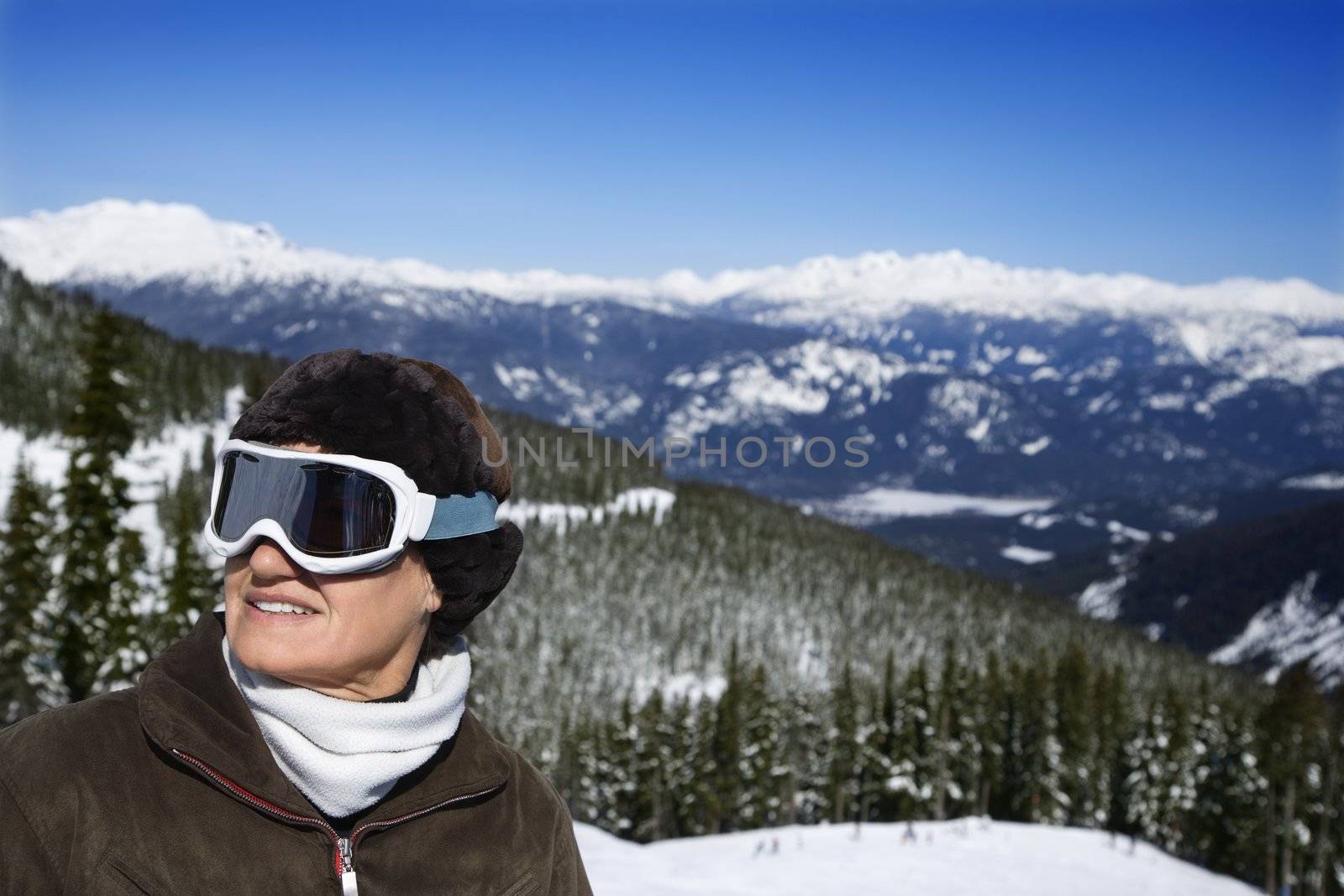 Caucasian middle-aged woman skier in goggles posing on mountain.