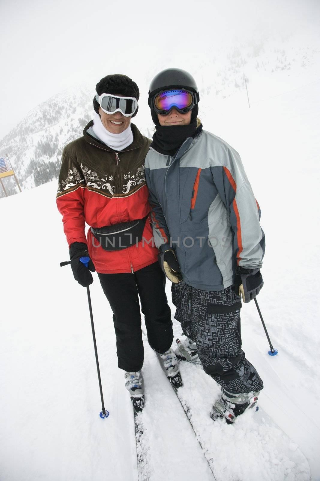 Middle-aged mother with teenage son on snowy ski slopes.