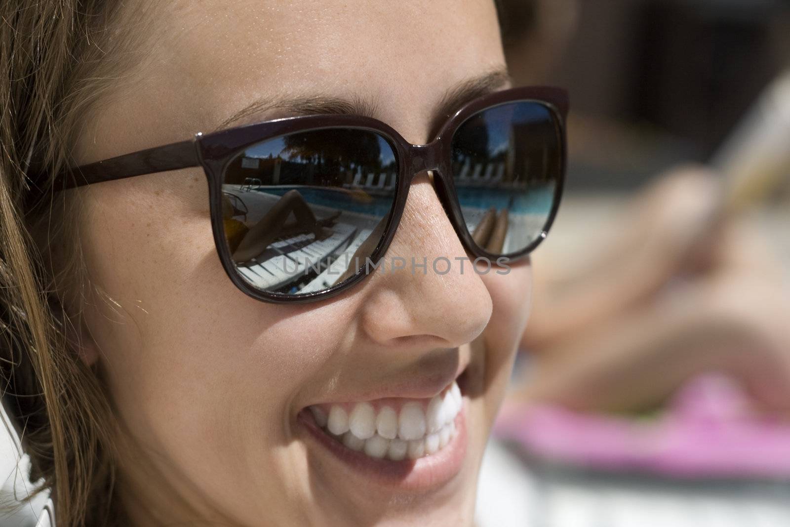 Happy young woman wearing sunglasses, with a reflextion of the pool.