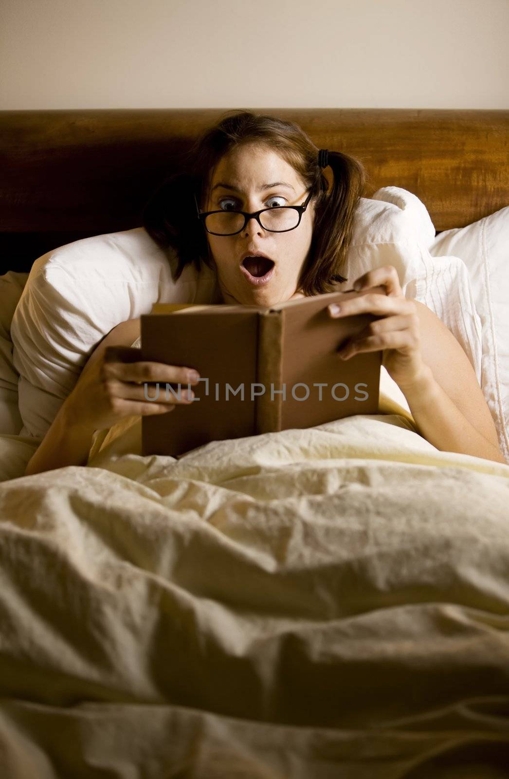 Woman reading in bed with a shocked expression
