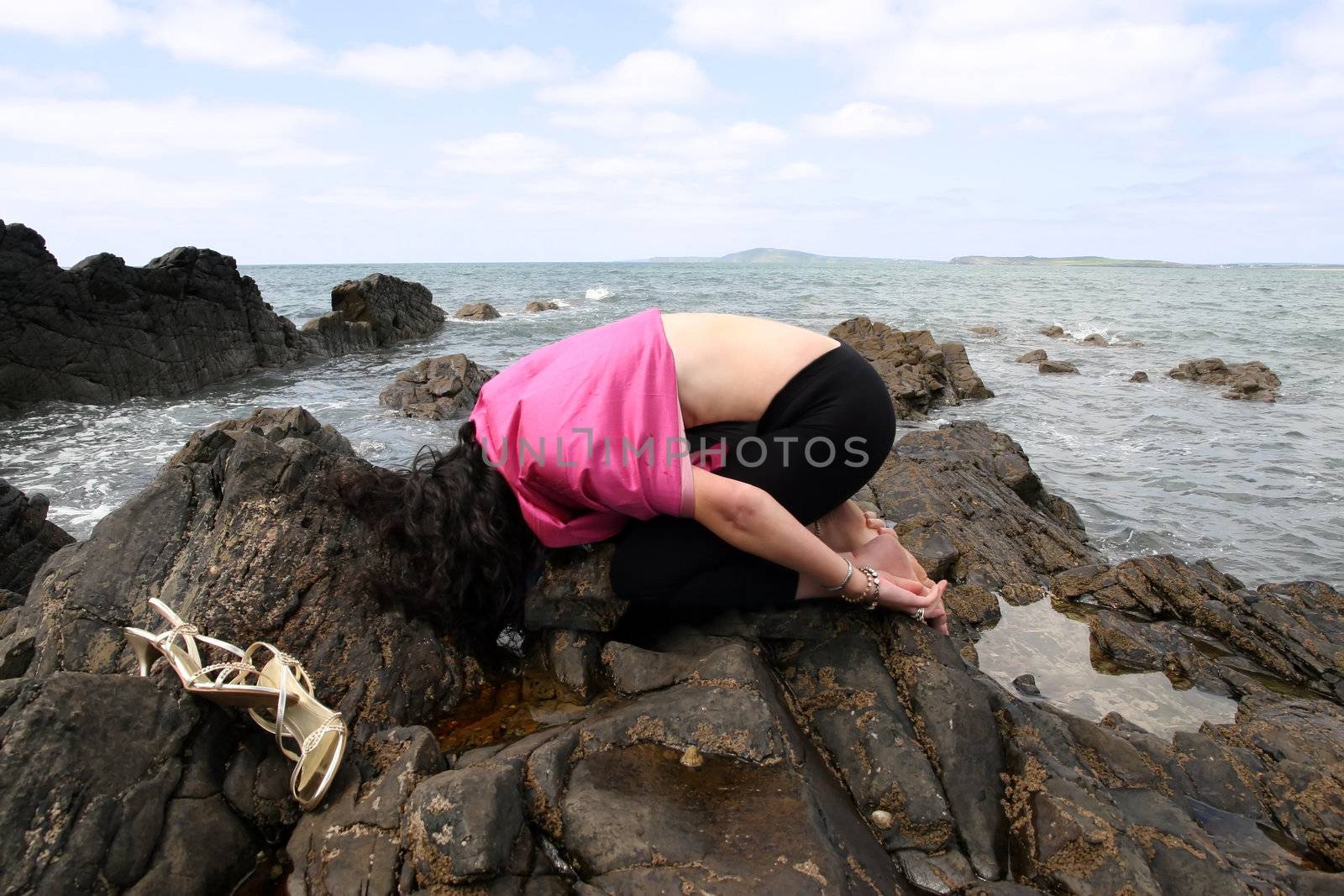 beautiful woman meditating on the rocks in ireland with her eyes closed, in a curled position, showing a healthy way to live a happy and relaxed lifestyle in a world full of stress