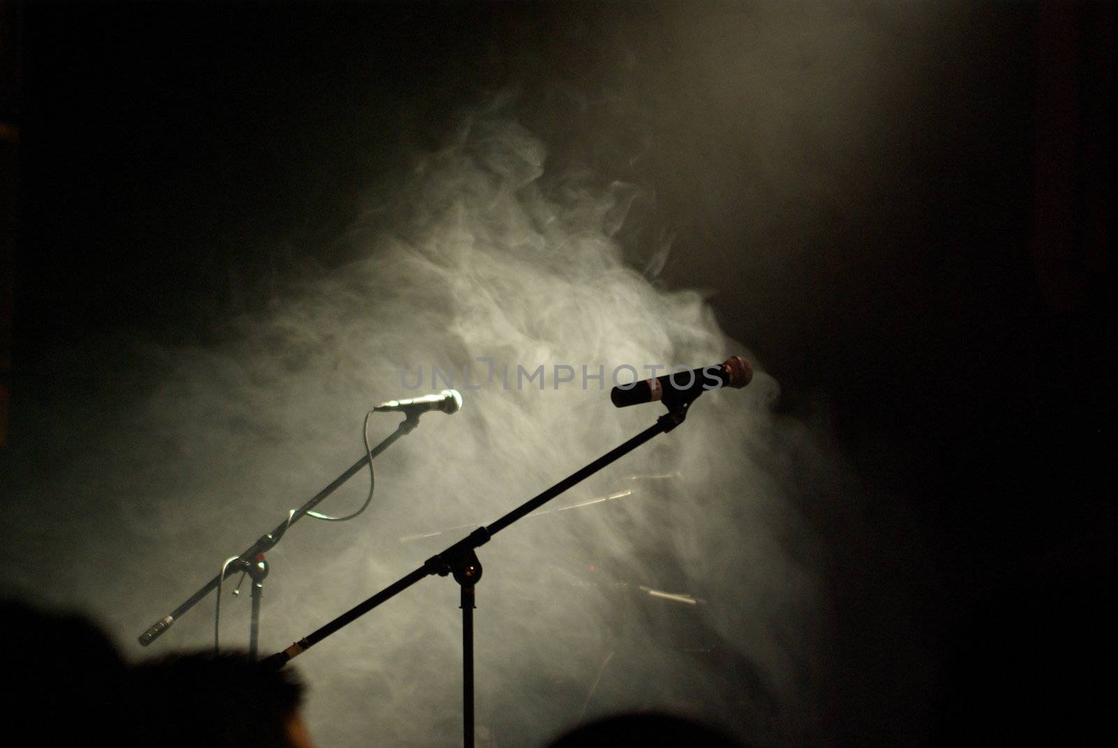 Two microphones standing in a cloud of smoke waiting for the band to arrive and start playing.