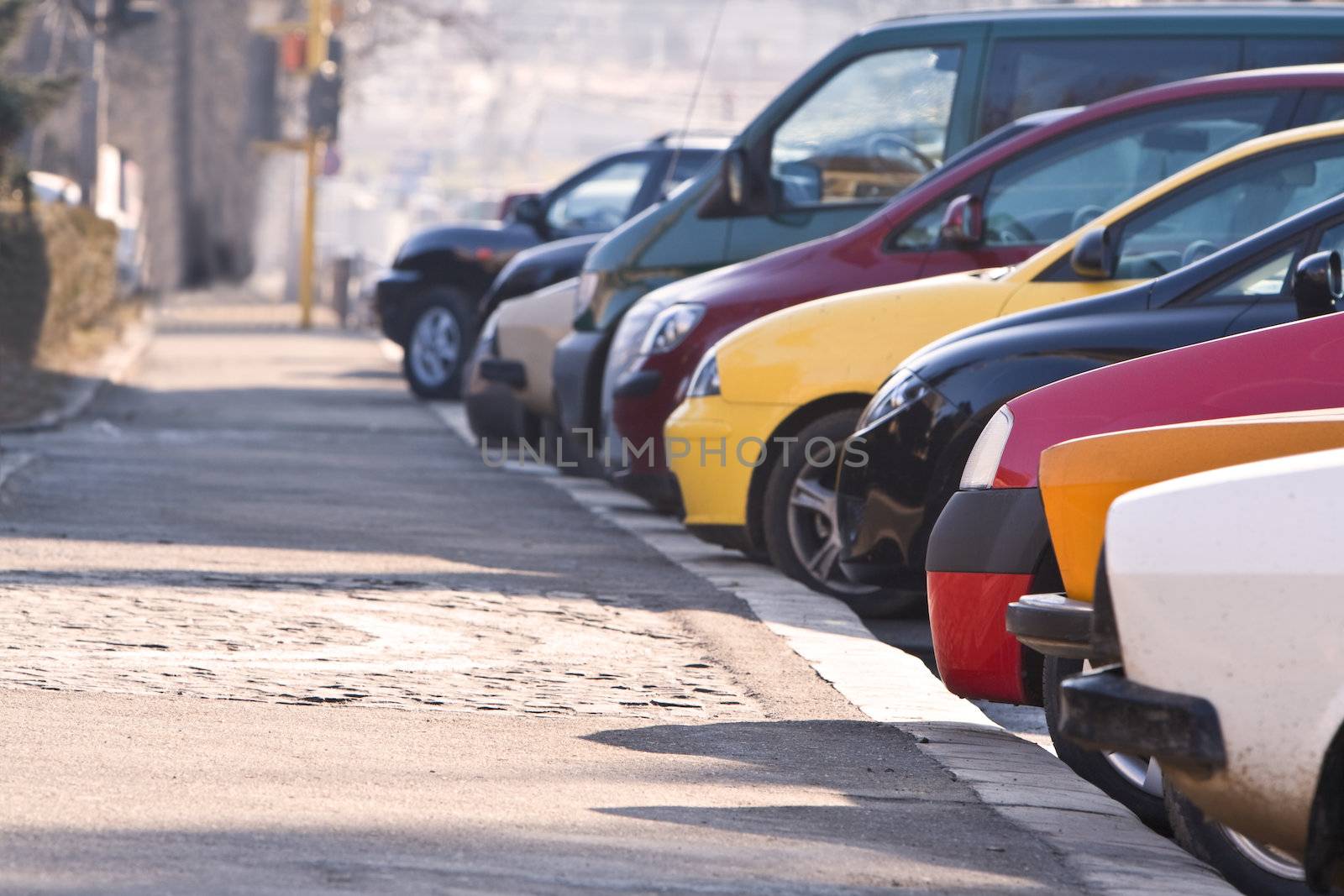 Row of different cars parked in a crowded city.