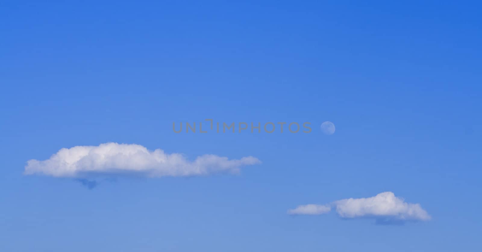 Clouds and moon on a blue sky in a late afternoon.