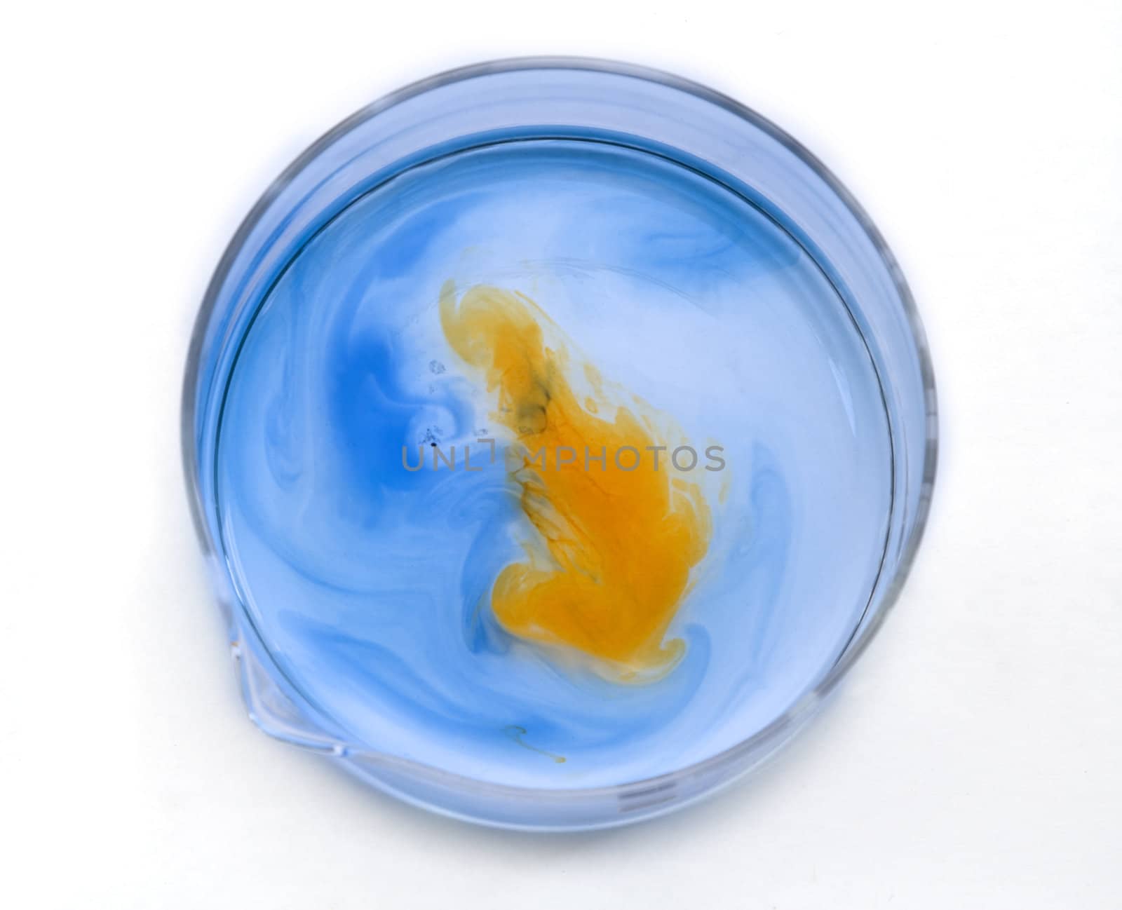 Blue and orange substances dissolving and blending in a glass recipient-upper view.