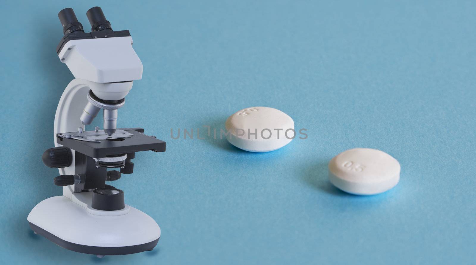 Two aspirin pills and a microscope on a blue surface with some shadows.