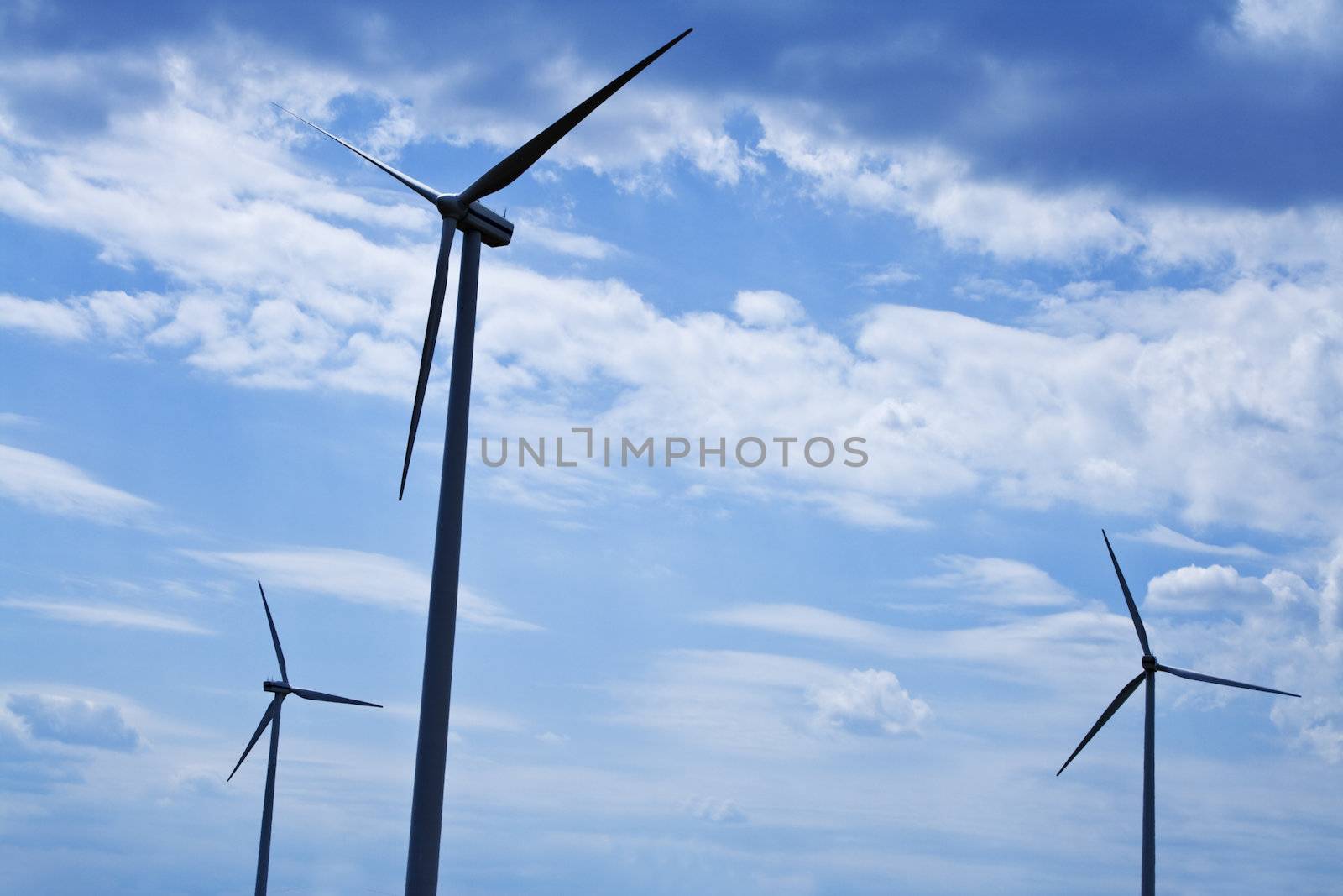 Silhouettes of eolian turbines against a cloudy sky.