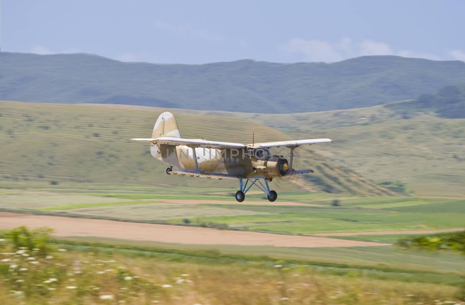 Panning image of a biplane flying in a mountain area during an airshow.