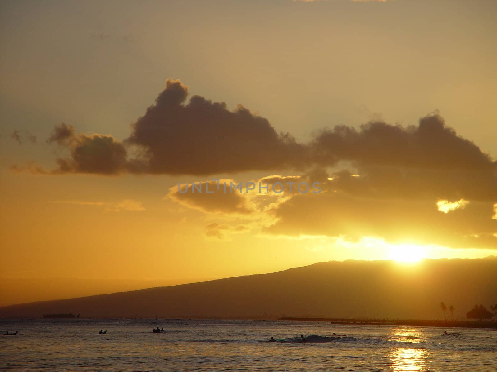 The sun setting over the island of Oahu and the surf on Waikiki Beach.