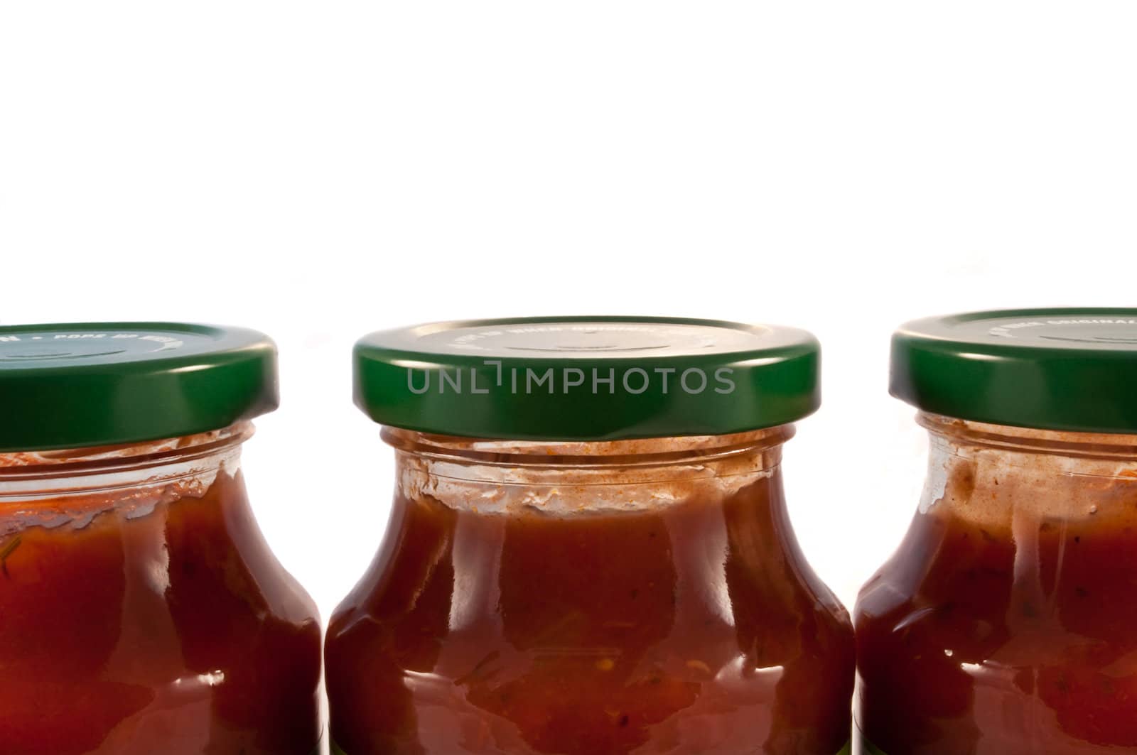 Close and low level angle capturing three glass jars with green lids filled with red pasta sauce and arranged horizontally with white background.