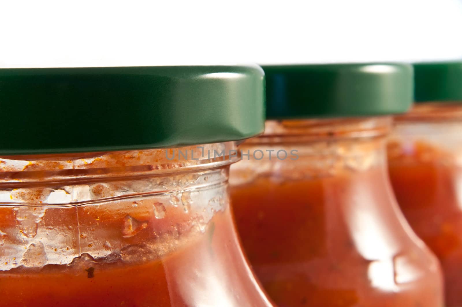 Close and low level capturing three pasta sauce filled glass jars in a line leading away from camera. Nearest jar in focus.