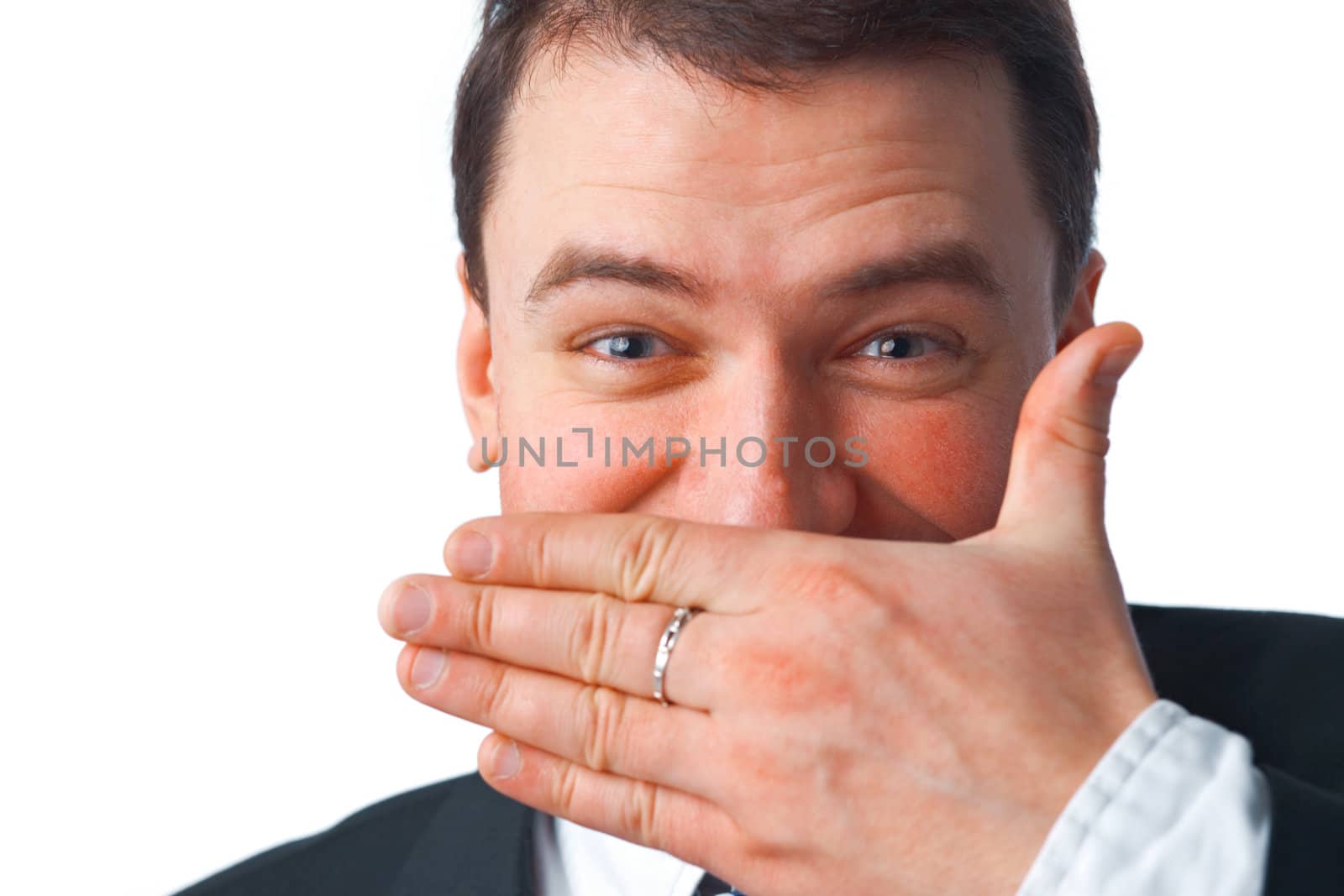 Close up portrait of young smiling businessman covering mouth with his hand while looking at you over white 