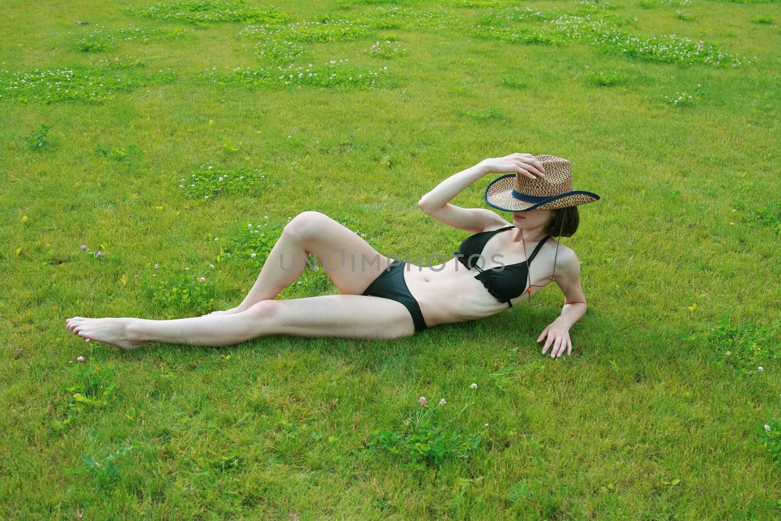 The girl in bikini sunbathes on a green lawn