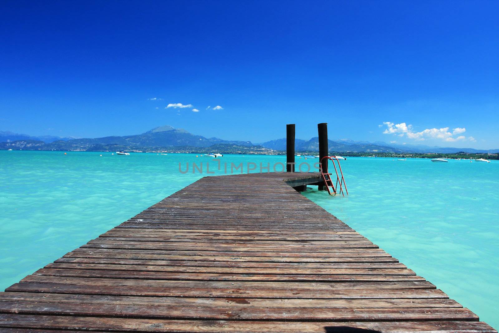 Small jetty in lake Garda Italy, fantastic blue color in sky and green invitin color of water. Perfect concept shot for any kind of vacation or tropics
